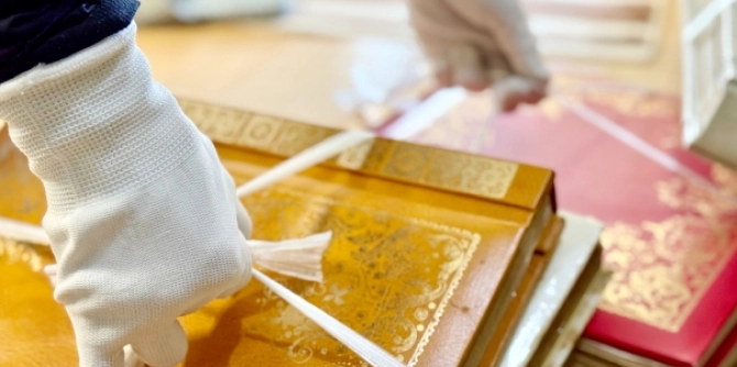 Person wearing white gloves handling gold-embossed antique books on a table, suggesting restoration or cataloging work.
