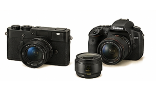 Two black cameras with a removable lens positioned between them on a light beige background.